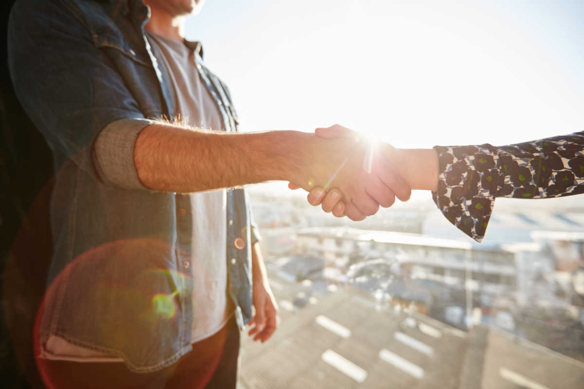 Closeup of shaking hands of man and woman with lens flare. Focus on handshake on a sunny day.